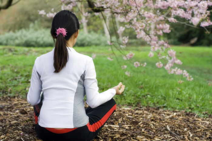 A woman sitting in meadow under a tree and meditating.