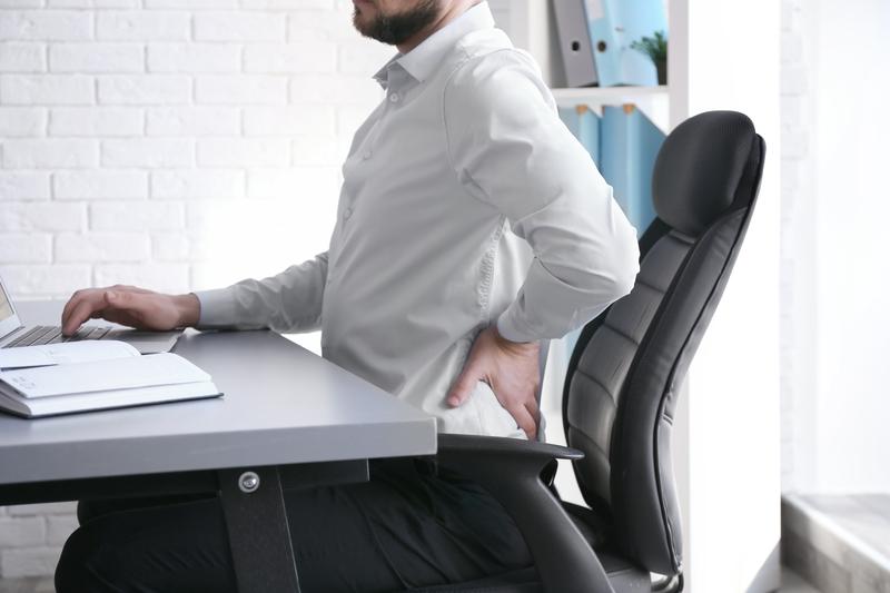 Man experiencing lower back postural strain while typing at an office desk